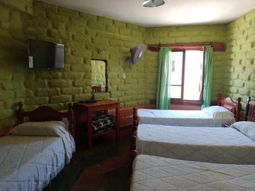 Habitación con 3 camas y TV en la pared. en Hotel El Jardin Dante en Tilcara