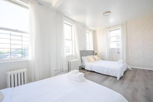 a white bedroom with two beds and two windows at Luxury NY Home close to NYC! in Yonkers