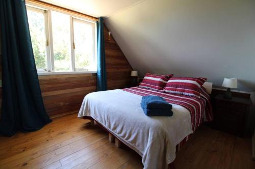 Schlafzimmer mit einem Bett mit roten Kissen und einem Fenster in der Unterkunft TuArriendoCL-Acogedora Cabaña Cercana a Playa Niklitschek hasta 5 PAX in Puerto Varas