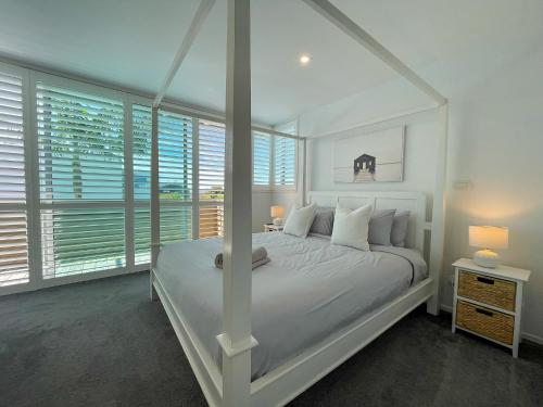 a white bedroom with a white bed and windows at Luxury Beachside Retreat in Papamoa