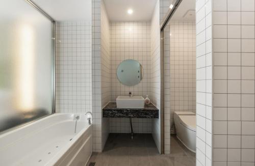 a white tiled bathroom with a tub and a sink and a mirror at Gimpo JK Hotel in Gimpo