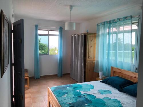 Schlafzimmer mit einem Bett mit blauen Vorhängen und einem Fenster in der Unterkunft Villa T4 Garden With See-view in Petit-Bourg
