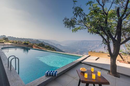 a swimming pool with a table and a view at SaffronStays Mountain Rizz in Panchgani