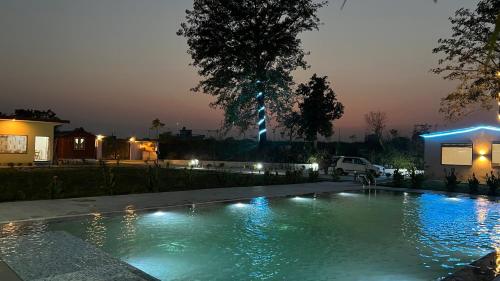 a swimming pool with lights in a yard at night at Wild Planet Corbett Hotel and Resort in Rāmnagar