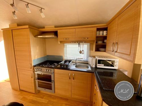 a kitchen with wooden cabinets and a sink and a microwave at Palm Grove 132 - pet friendly, WiFi, central heating, close to shops and beach - Meadow Lakes Caravan & Lodge Hire in Chapel Saint Leonards