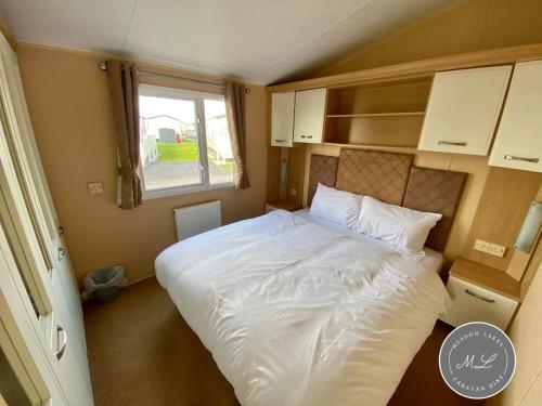a bedroom with a large white bed with a window at Palm Grove 132 - pet friendly, WiFi, central heating, close to shops and beach - Meadow Lakes Caravan & Lodge Hire in Chapel Saint Leonards