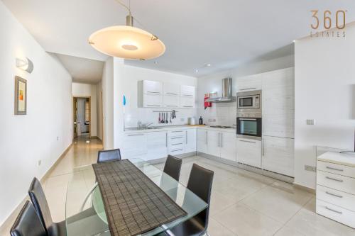 a white kitchen with a glass table and chairs at Beautiful seafront home with private balcony & BBQ by 360 Estates in Tal-Pietà