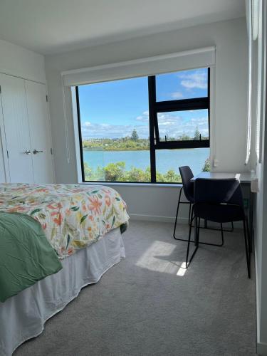 a bedroom with a bed and a desk and a large window at Relax by the Tamaki River in Auckland