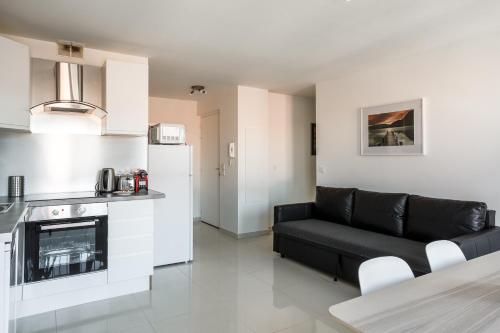a living room with a black couch and a kitchen at Le blanc mesnil 23 Abbé niort 1er ETG gauche in Le Blanc-Mesnil