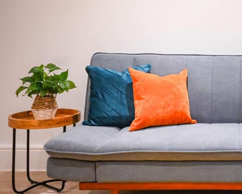 a blue couch with an orange pillow and a table at Luxury 2 Bed Maisonette with Parking Near Tube in London