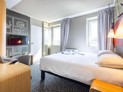 a hotel room with a bed and a desk with a laptop at ibis Saint Malo Plage in Saint Malo