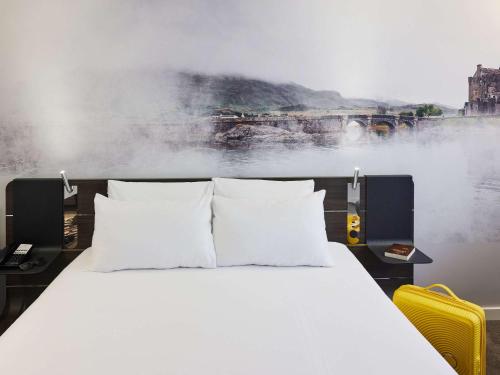 1 cama con almohadas blancas en una habitación con una pintura en Novotel Edinburgh Centre, en Edimburgo