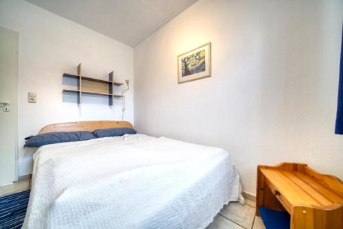 Schlafzimmer mit einem weißen Bett und einem Holztisch in der Unterkunft Haus am See, App 3HAS06 in Heiligenhafen
