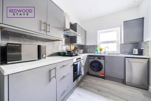 cocina con armarios blancos, lavadora y secadora en BRAND NEW, 2 Bed 1 Bath, Modern Town Center Apartment, FREE WiFi & Netflix By REDWOOD STAYS en Aldershot