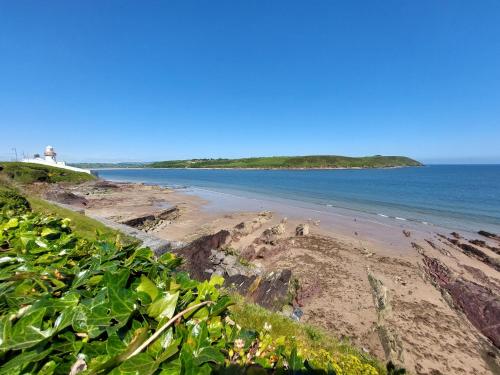 a view of a beach with a lighthouse in the background at Sea Whispers - My Charming Costal Retreat in Youghal in Youghal