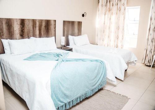 2 letti in una camera da letto con lenzuola bianche e coperta blu di Conmilla Guest House and Conference Venue a Berea Hills