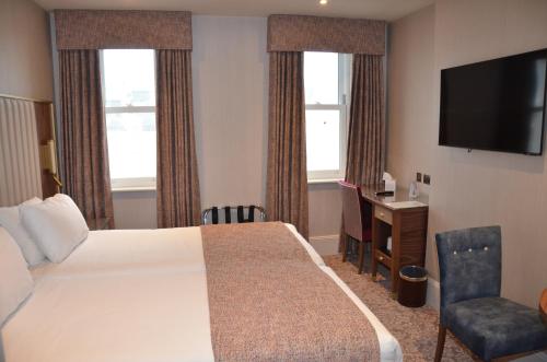 a hotel room with a bed and a desk and a television at voco The Clifton Folkestone by IHG in Folkestone