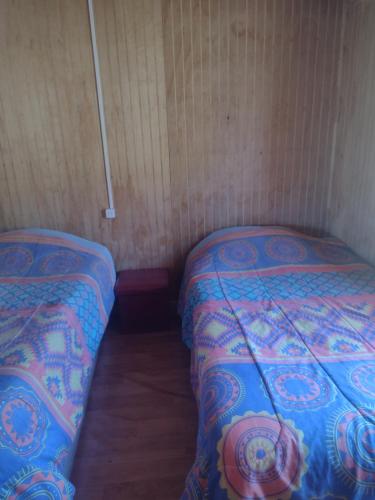 two beds in a small room with wooden walls at Cabaña bellavista in Cochamó