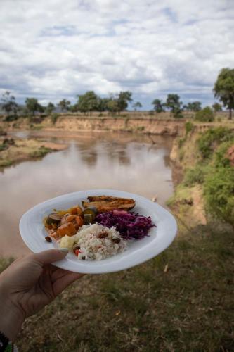 a person holding a plate of food in front of a river at Olimba Mara Camp in Mara Simba