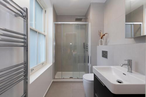 uma casa de banho branca com um chuveiro e um lavatório. em Deluxe North Central London Apartment em Londres