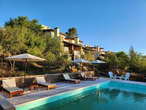 una piscina con sillas y sombrillas junto a un edificio en Terrazas de Piedra en Santa Rosa de Calamuchita