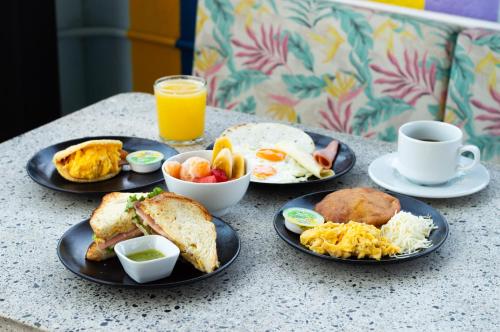 uma mesa com pratos de alimentos para o pequeno-almoço e uma chávena de sumo de laranja em Mythical Hotel - Boutique em Medellín