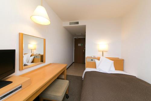 a hotel room with a bed and a desk and a television at Smile Hotel Shizuoka in Shizuoka