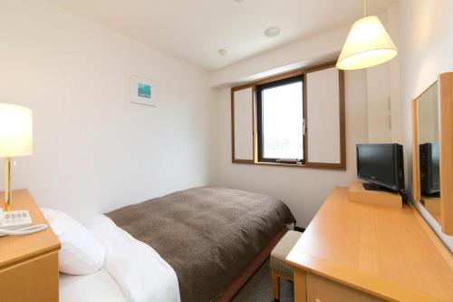 a bedroom with a bed and a desk with a television at Smile Hotel Shizuoka in Shizuoka