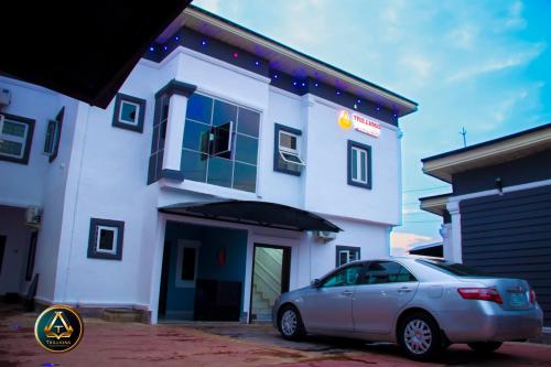 un edificio blanco con un coche aparcado delante de él en TRILLIONS HOTEL AND APARTMENT, en Benin City