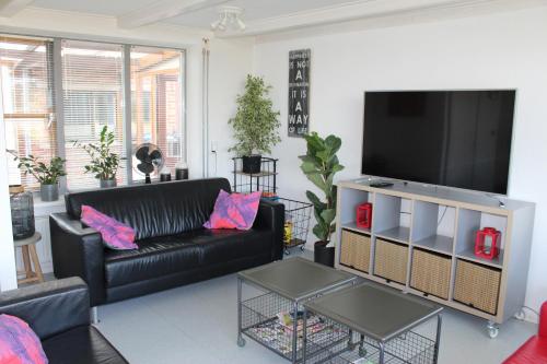 a living room with a black couch and a flat screen tv at vrijstaande ruime familiewoning landelijk gelegen in Lewedorp