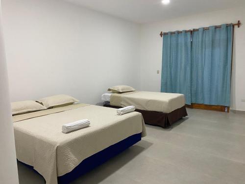 two beds in a room with blue curtains at Penguin House in Puerto Villamil