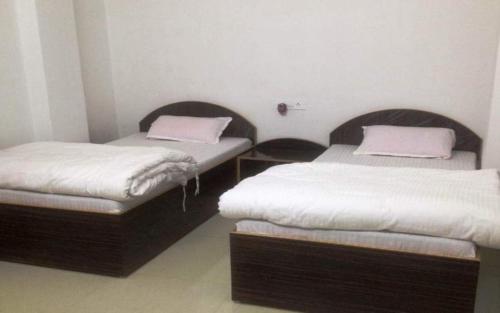 Duas camas individuais num pequeno quarto com lençóis brancos. em RK GUEST HOUSE em Bodh Gaya