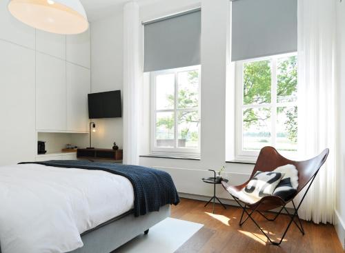 een slaapkamer met een bed, een stoel en ramen bij Het Raadhuys - design B&B in Kessel