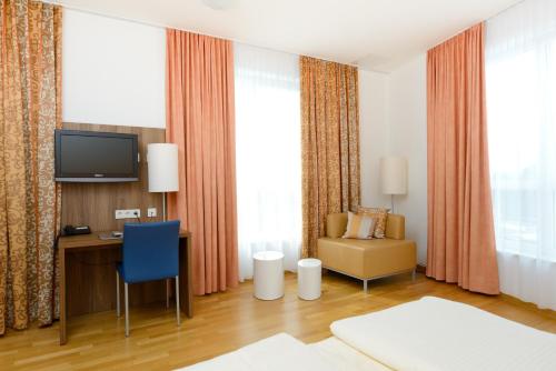 ein Hotelzimmer mit einem Schreibtisch, einem TV und einem Stuhl in der Unterkunft Zar-Hotel Vitalis in Regensburg