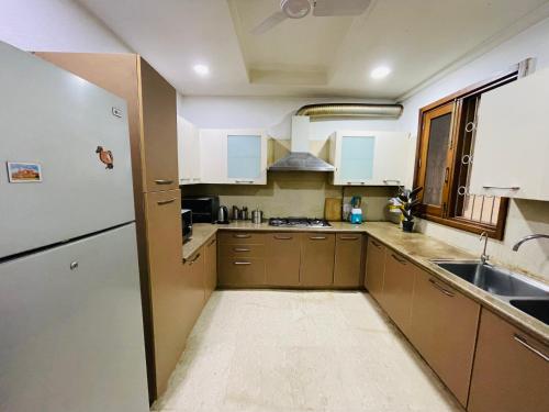 La cuisine est équipée de placards bruns et d'un réfrigérateur blanc. dans l'établissement Fortune Home Service Apartment 4Bhk,J-191 Saket, à New Delhi