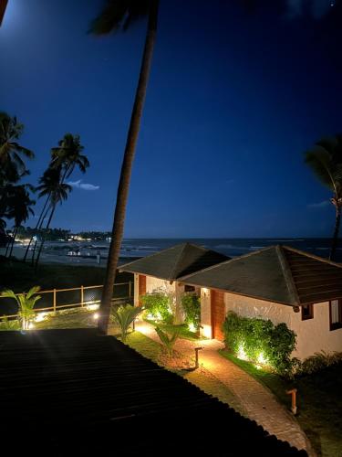 a house with lights in front of the ocean at night at Joju Bangalôs & Bistrô in Japaratinga