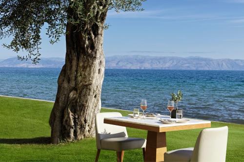 a table with wine glasses and chairs next to a tree at Domes Miramare, a Luxury Collection Resort, Corfu - Adults Only in Moraitika