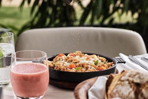 a table with a pan of food and a glass of water at Domes Miramare, a Luxury Collection Resort, Corfu - Adults Only in Moraitika