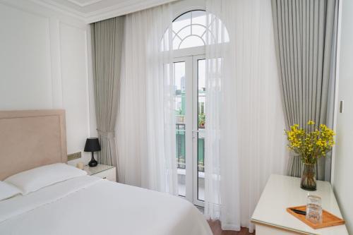 a white bedroom with a bed and a window at The Nguyens - Pink Church View in Ho Chi Minh City