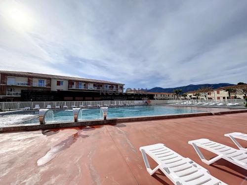 une piscine avec deux chaises blanches et un bâtiment dans l'établissement 2950-Appartement une chambre avec piscine, à Argelès-sur-Mer