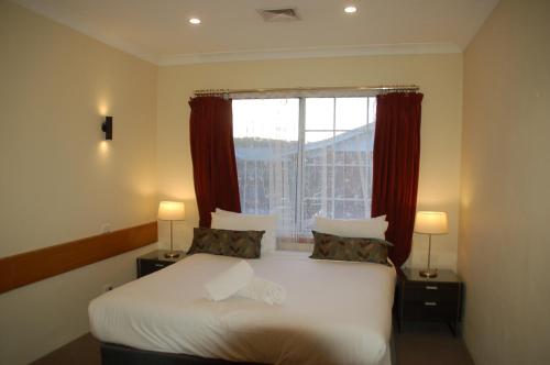a bedroom with a bed and a window with red curtains at Meramie Motor Inn in Albury