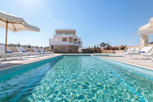 a swimming pool with chairs and an umbrella at Anna Mare Luxury Apartments in Afitos
