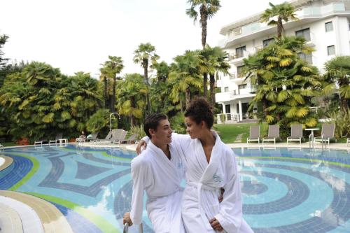 two women in white robes standing in front of a swimming pool at Parc Hotel Flora S in Riva del Garda