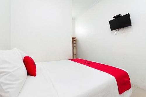 a white bed with red pillows and a tv on a wall at RedDoorz Syariah near RSUD Zainoel Abidin Banda Aceh in Banda Aceh