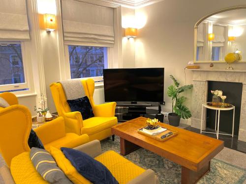 a living room with yellow furniture and a television at Beaufort Gardens Apartment in Knightsbridge in London