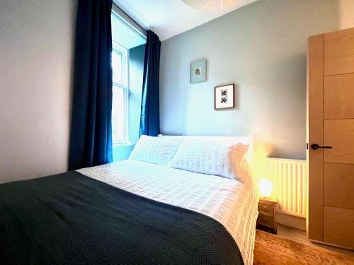 a bedroom with a bed with blue curtains and a window at Garden Flat in Edinburgh