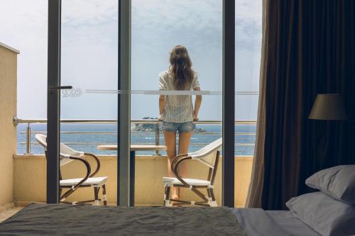 a woman looking out of a window at the ocean at Hotel Palas in Petrovac na Moru