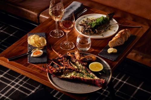 uma mesa de madeira com dois pratos de comida e copos de vinho em Hilton Adelaide em Adelaide