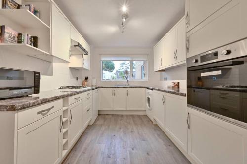a white kitchen with white cabinets and a window at Spacious Sandbanks Apartment near Beach and Bars with Free Parking in Poole
