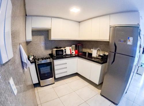La cuisine est équipée de placards blancs et d'un réfrigérateur en acier inoxydable. dans l'établissement casa de veraneio - casa 9 - condomínio azul mar - Porto de Galinhas, à Porto de Galinhas